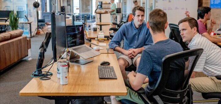 Tres hombres hablando frente a un monitor