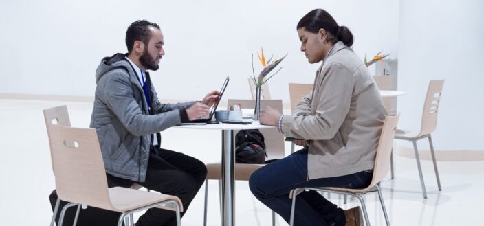 Pareja sentada en una pequeña mesa de café y mirando portátil y teléfono