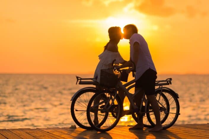 Pareja besándose al atardecer mientras sostiene sus bicicletas