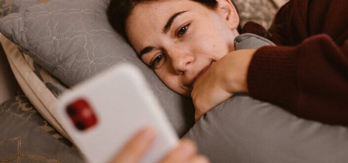dama acostada en su cama y mirando su teléfono