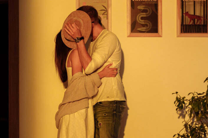 una pareja cubriendo sus rostros con un sombrero mientras se besan