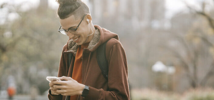 Hombre con auriculares y cabello recogido sonriendo sobre algo en su fone