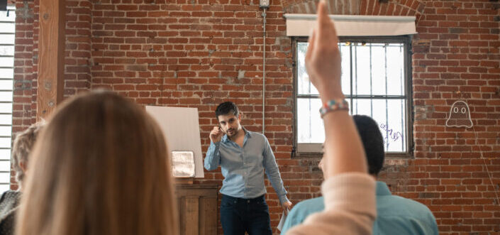 A man gesturing to accept questions from his audience.