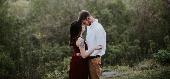 Una pareja vestida formalmente que tiene un momento romántico en el bosque.