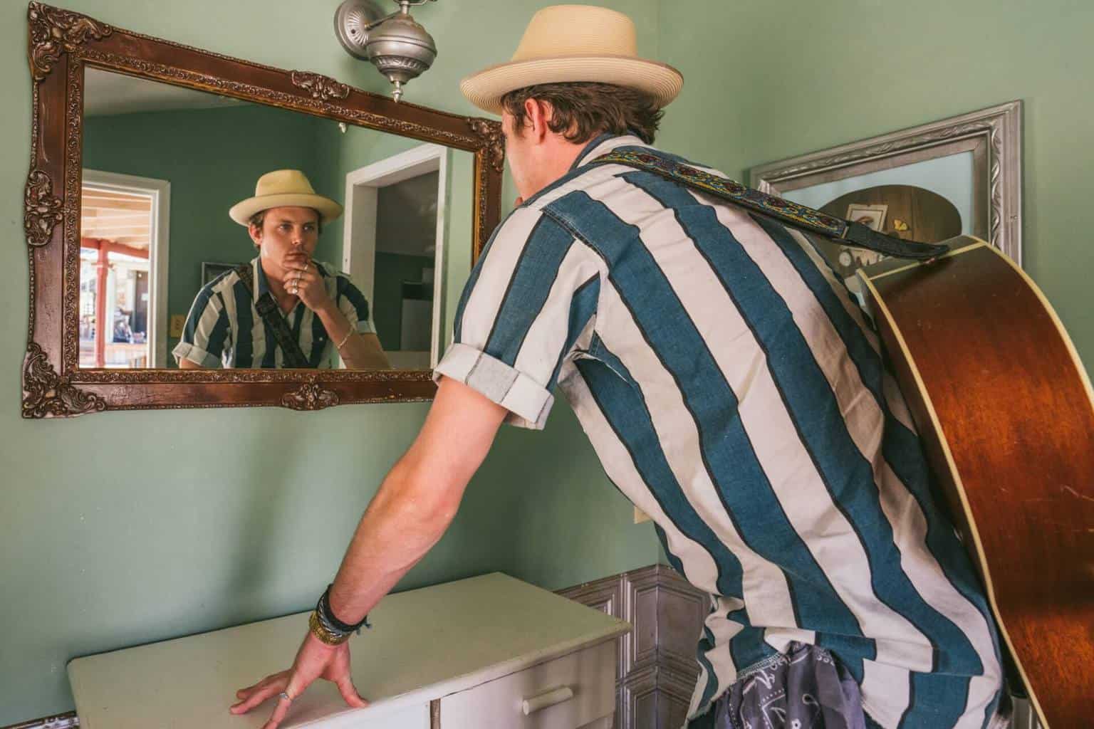 Man with a guitar checking himself in the mirror - featured