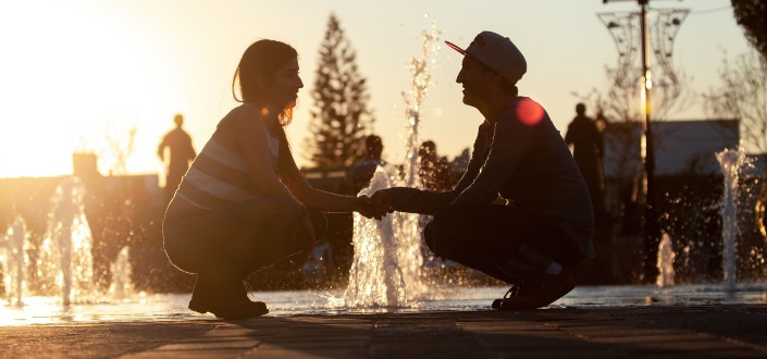 Pareja sentada en cuclillas mientras se abrazan frente a una fuente de agua