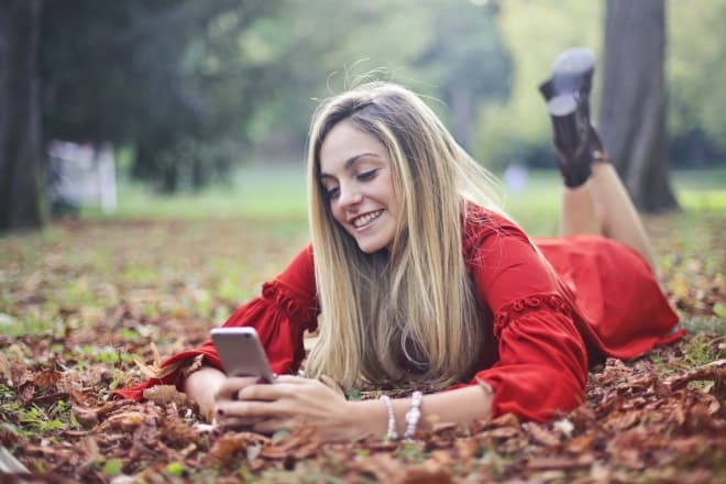 Mujer sonriente acostada sobre hojas secas mientras envía mensajes de texto - dares over text