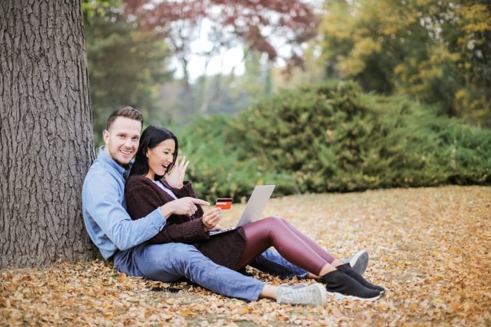  Pareja sentada bajo el árbol mientras compra online con su tarjeta de crédito
